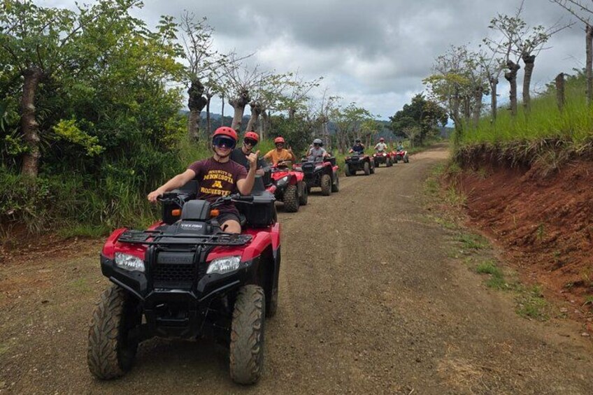 A group of people riding ATVs on a dirt road surrounded by trees. 5