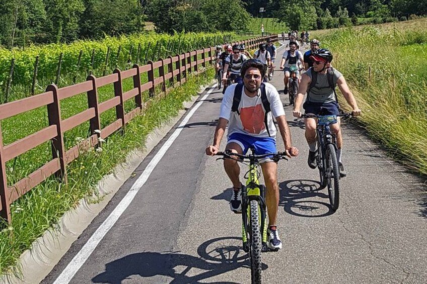 Cyclists on a paved path with a wooden fence on one side and green fields on the other. 4