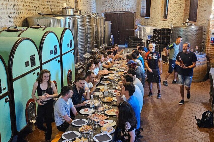 A group of people dining at a long table in a rustic setting with vintage-style refrigerators and wine barrels. 5