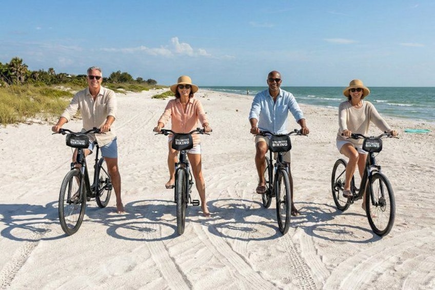 Four people riding bicycles on a sandy beach with ocean in the background. 3