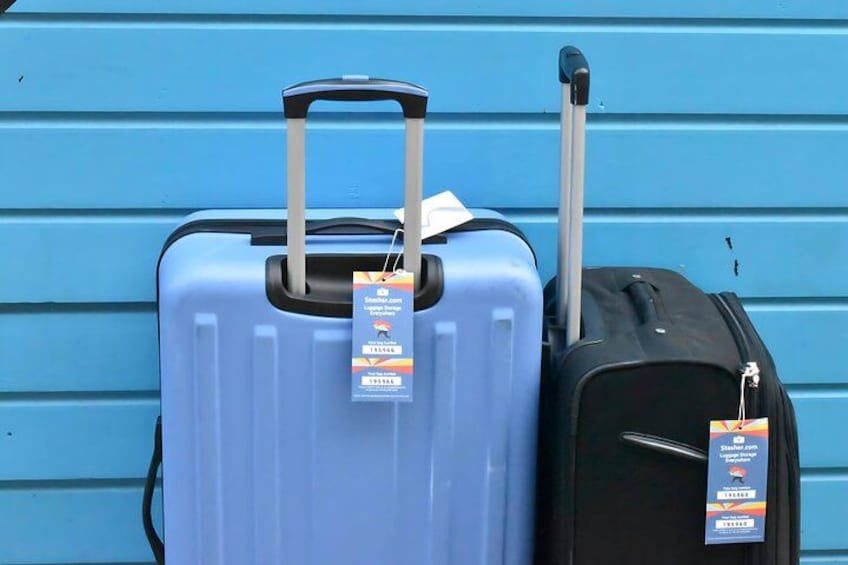 Two suitcases, one blue and one black, with tags against a blue wall. 1