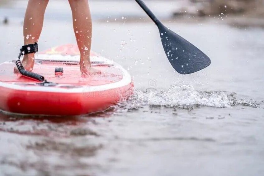 A person standing on a red paddleboard in water, using a black paddle. 2