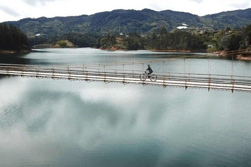 A person riding a bicycle on a bridge over a calm lake with mountains in the background. 3