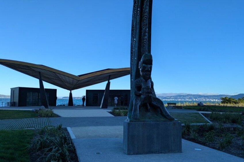 A modern architectural structure with a unique roof design, a large sculpture, and a view of the sea in the background. 4