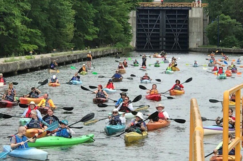 A group of people kayaking on a river with a bridge in the background. 1