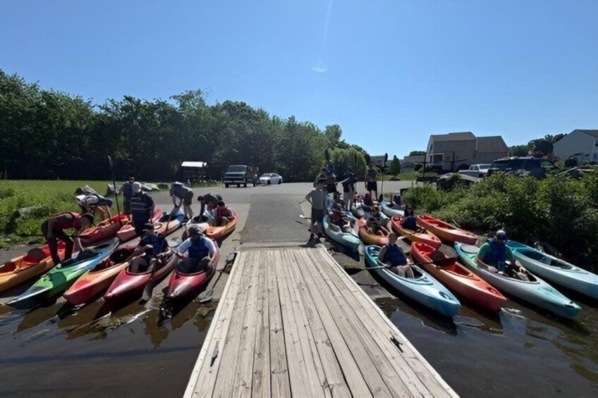 A group of people in canoes on a wooden dock by a calm body of water. 2