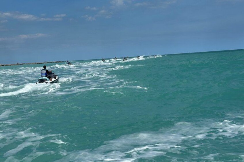 A person riding a jet ski on turquoise ocean waters with other jet skis in the distance. 2