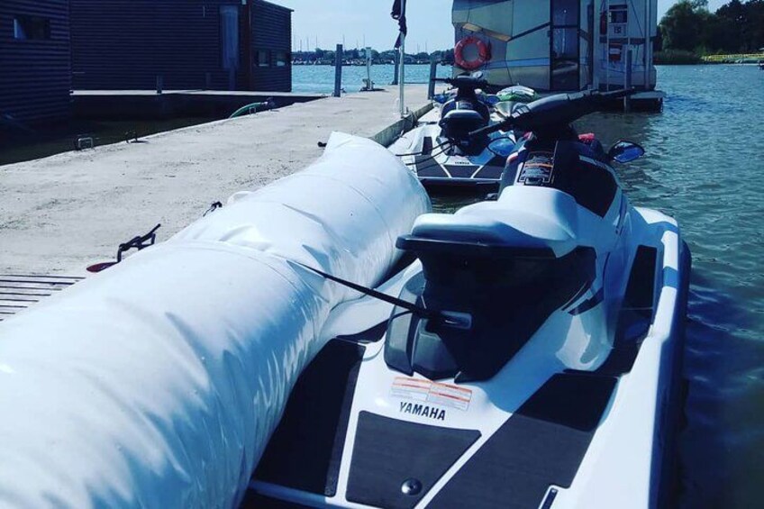 A white Yamaha jet ski docked at a marina with a boat in the background. 2