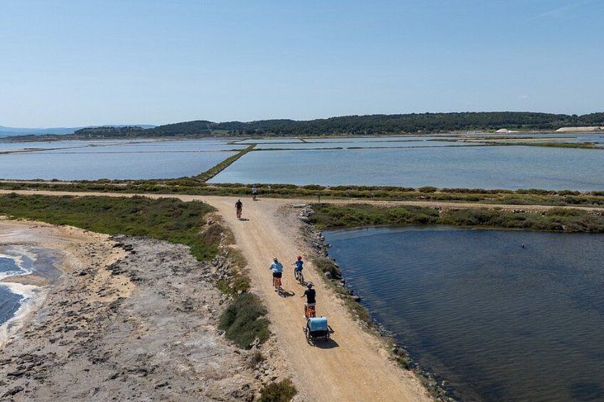 A coastal road with people walking and cycling, surrounded by water bodies and distant hills. 2