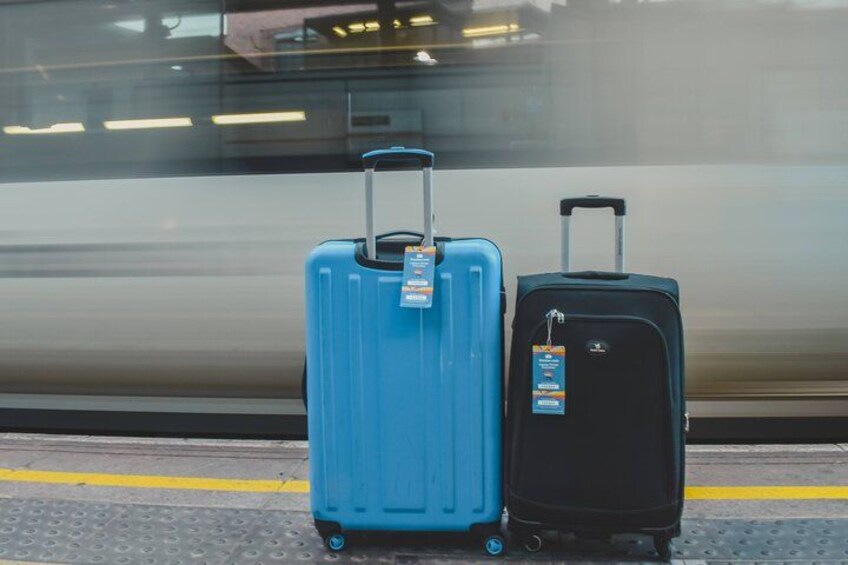 Two suitcases on a platform with a moving train in the background. 5