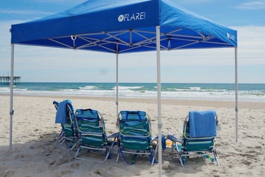 A beach with a blue canopy labeled 'FLAREI' and three beach chairs with towels. 2