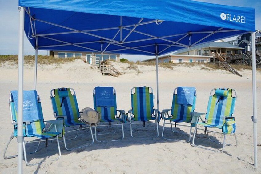 A beach with a blue canopy and beach chairs. 1
