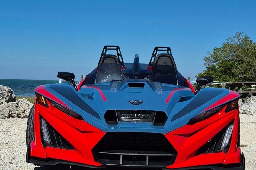 A red and blue sports car parked on a beach with a clear sky. 1