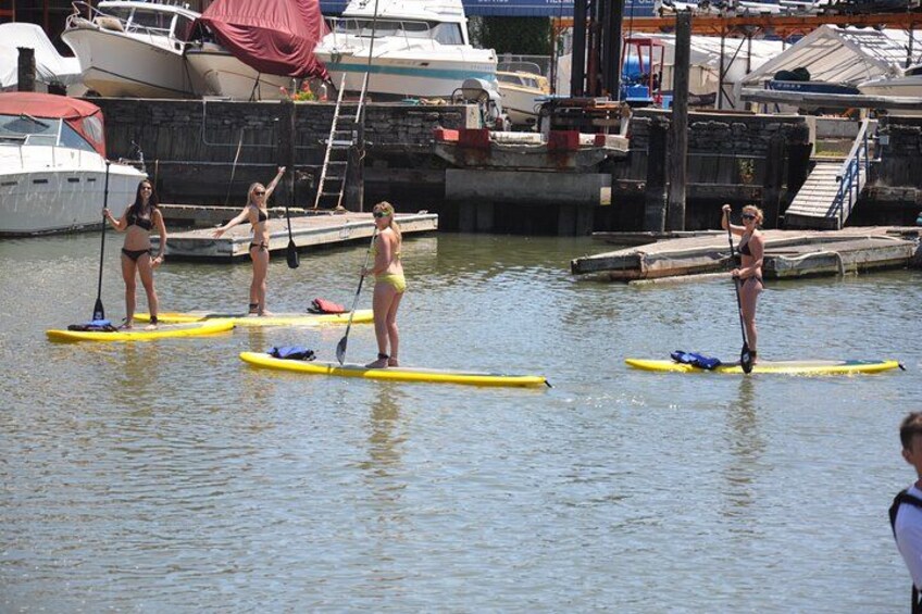 People paddleboarding on a calm body of water with boats docked in the background. 1