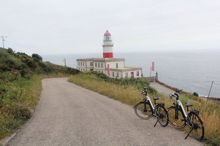 A coastal road with a lighthouse, bicycles, and a building. 1