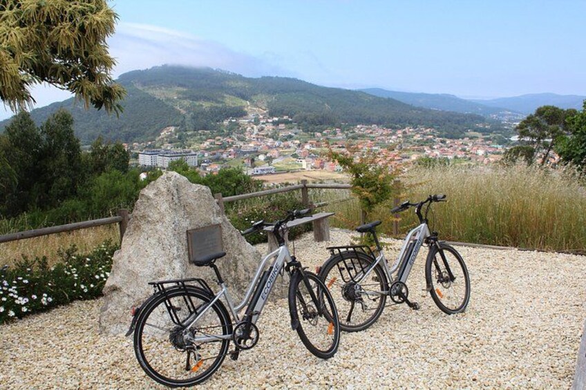 A gravel path with bicycles parked on it, overlooking a town with buildings and hills in the background. 4