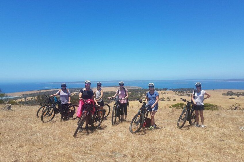 A group of cyclists on a hilltop with a view of the ocean. 2