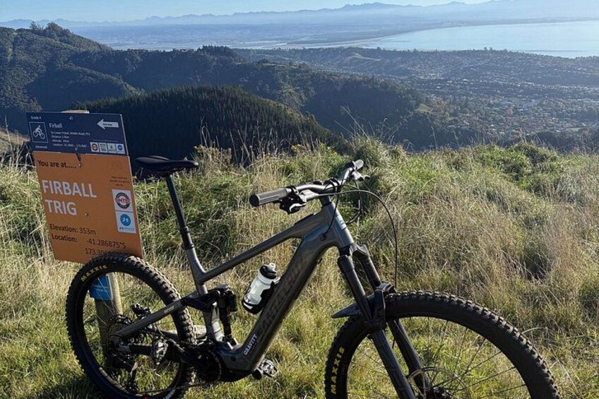 A mountain bike parked on a grassy hill with a sign indicating a location at 353m elevation. 2