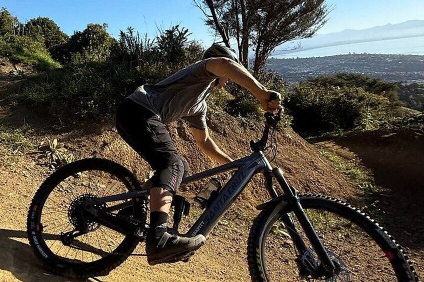A person riding a mountain bike on a dirt trail with a scenic view of a body of water and hills in the background. 1
