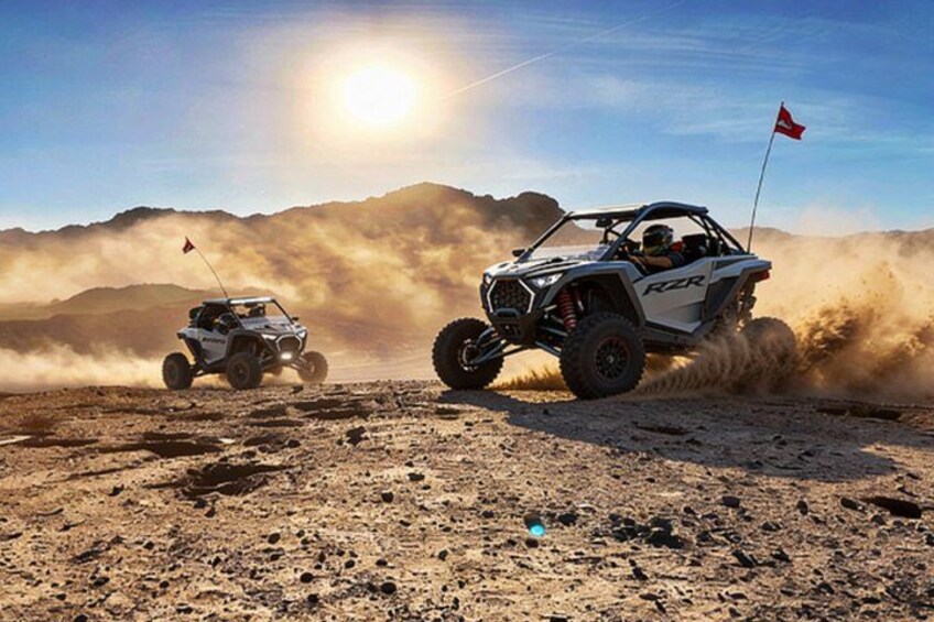 Two off-road vehicles on a dusty terrain with mountains in the background. 5