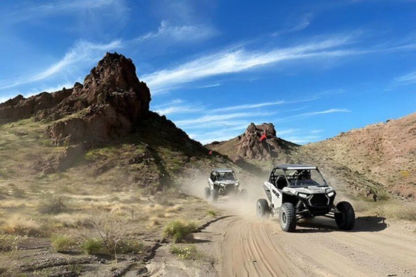 Off-road vehicles on a dirt road with rocky terrain and clear skies. 4