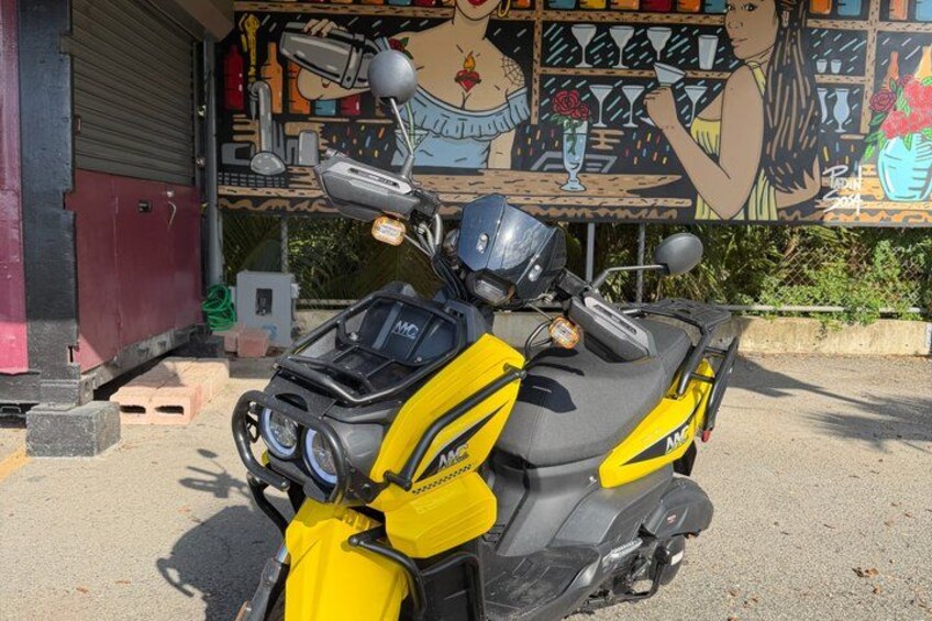 A yellow and black motorcycle parked in front of a building with a mural. 2