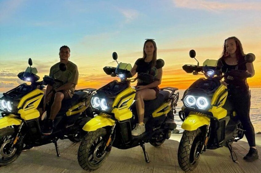Four people sitting on yellow scooters with a sunset in the background. 1
