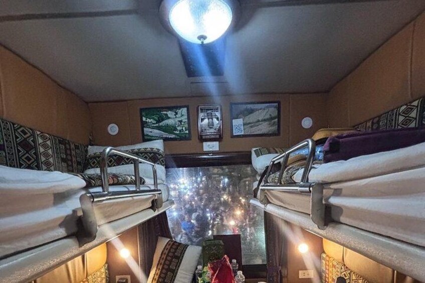 A train compartment with bunk beds, a central aisle, and overhead lighting. 4
