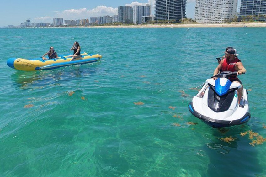 A jet ski and a raft in clear turquoise water with a city skyline in the background. 5