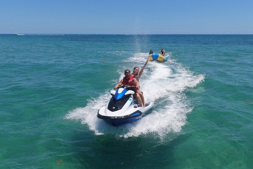 A jet ski with two people riding it, another jet ski in the background, and calm blue ocean water. 4