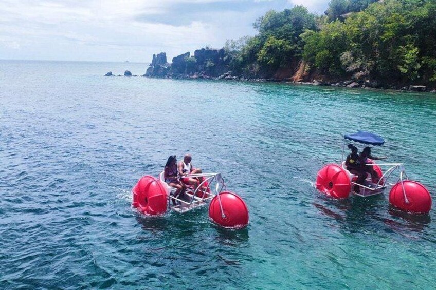 Two people on a red watercraft with large wheels, floating on clear blue water. 5