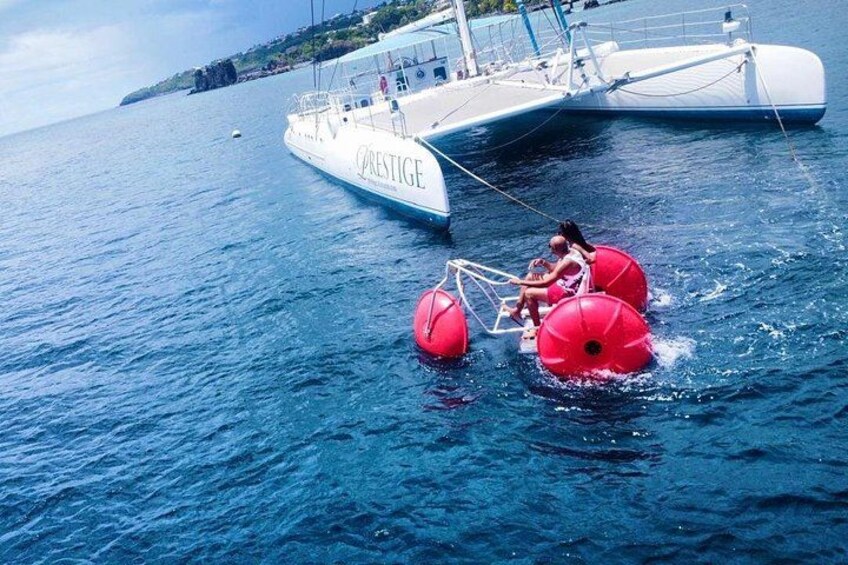 A boat named 'PRESTIGE' with two people riding red inflatable devices in the water. 1