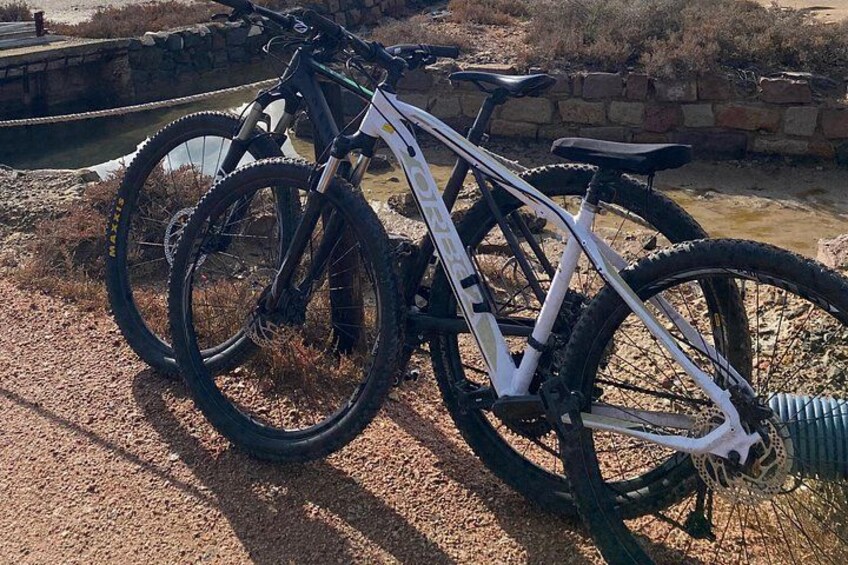 A mountain bike parked on a gravel path with a stone wall and a small water body in the background. 1
