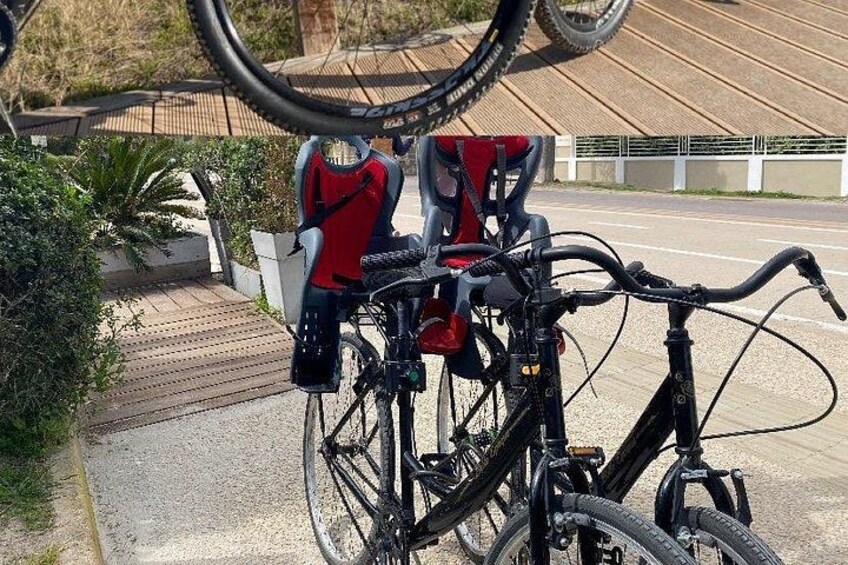 A bicycle with a red seat and black frame, parked on a sidewalk with a road in the background. 3