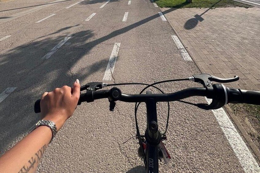 A hand gripping a bicycle handlebar, with a road and a sidewalk in the background. 5