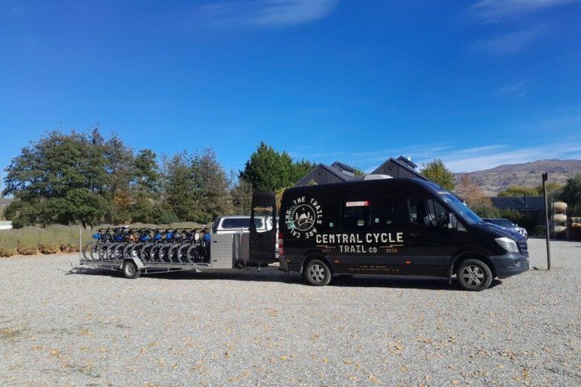 A black van with 'Central Cycle Trail Co' written on it, parked on a gravel surface with a trailer attached. 2