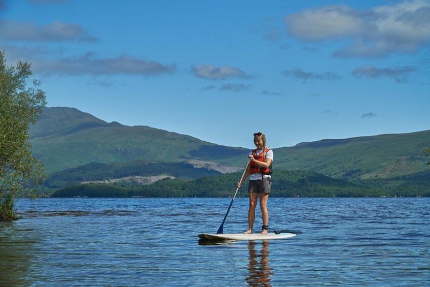 A person paddleboarding on a calm lake with mountains in the background. 1