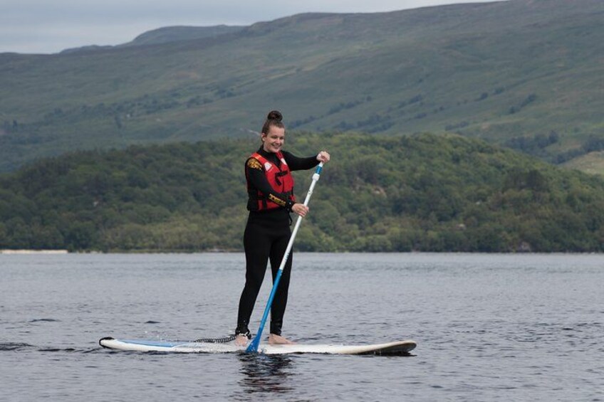 A person paddleboarding on a calm lake with hills in the background. 3