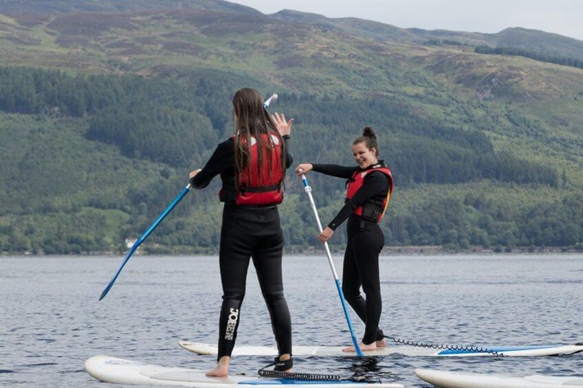 Two people paddleboarding on a calm lake with mountains in the background. 2