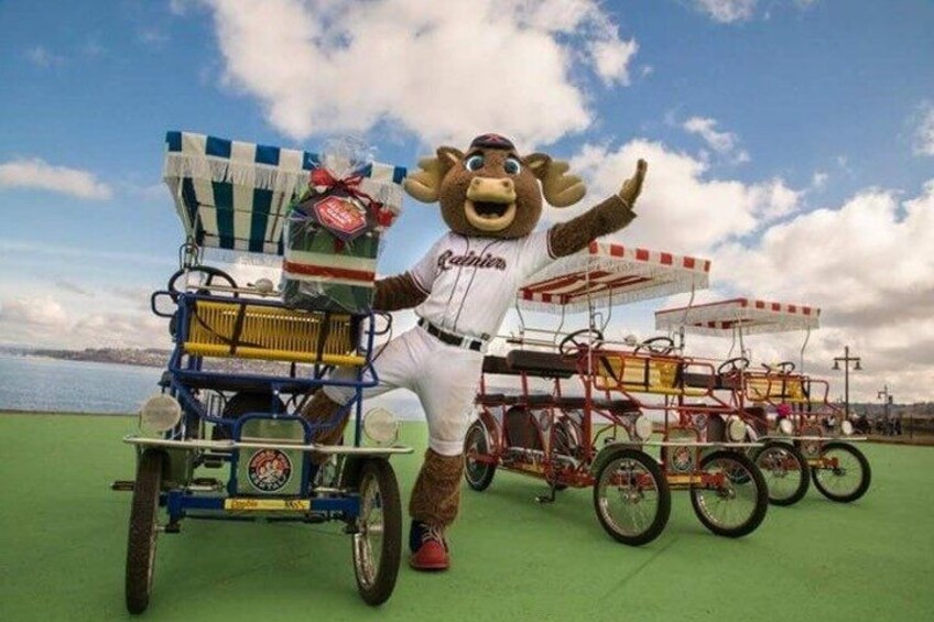 A mascot in a white uniform with a red belt, standing next to a blue and yellow cart with a striped canopy, and several red and yellow carts in the background. 3
