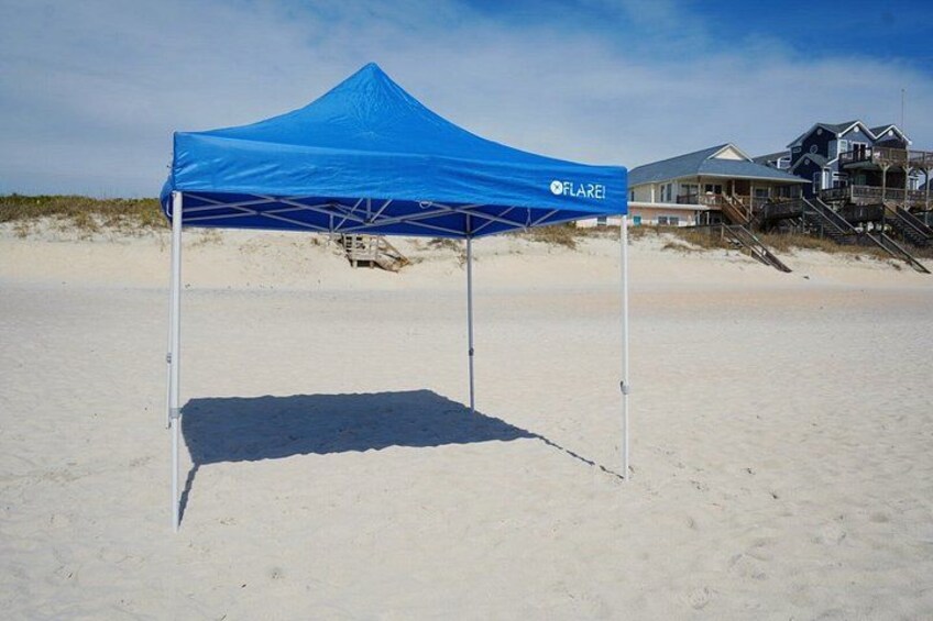 A blue tent on a sandy beach with a house in the background. 1