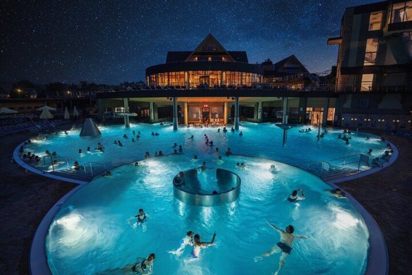 A large outdoor swimming pool at night with people swimming and relaxing. 1