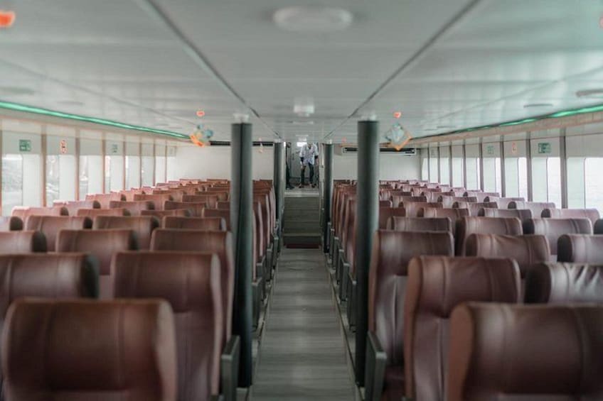 A ship's interior with rows of brown leather seats, a central aisle, and windows on both sides. 2