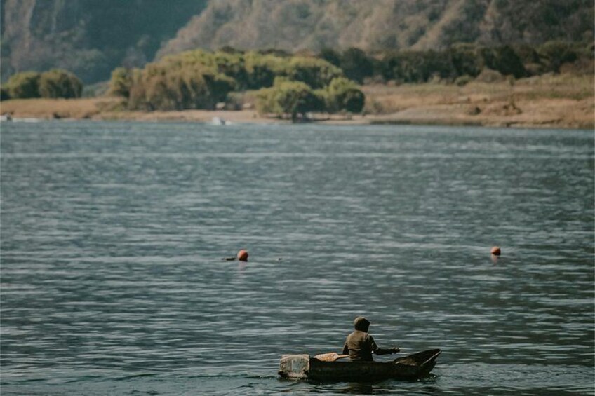 A person in a boat on a calm body of water with distant land and trees. 3