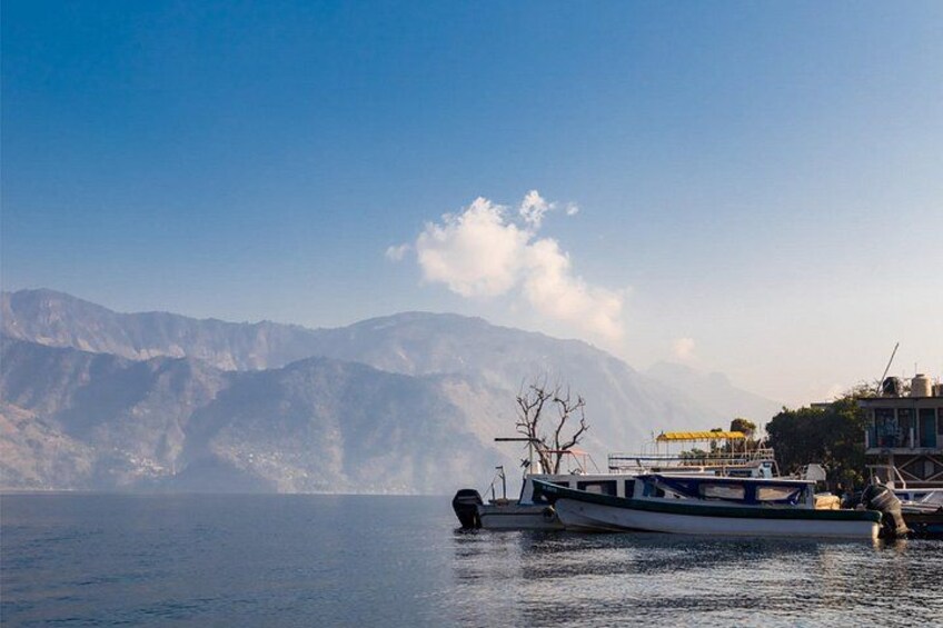 A calm lake with boats, a mountain range in the background, and a building with a yellow awning. 5