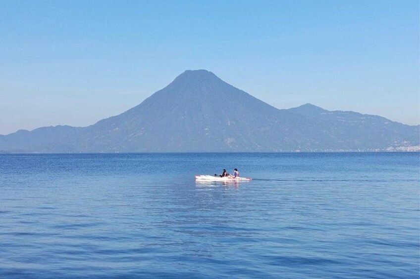 A calm sea with a boat carrying people, a mountain in the background, and a clear sky. 2