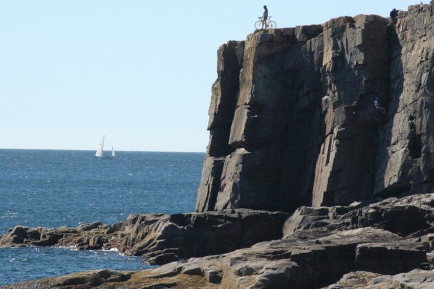 A rocky coastline with a sailboat in the distance and a bicycle on a cliff. 5
