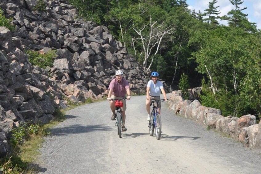 Two cyclists on a gravel road surrounded by rocks and trees. 1