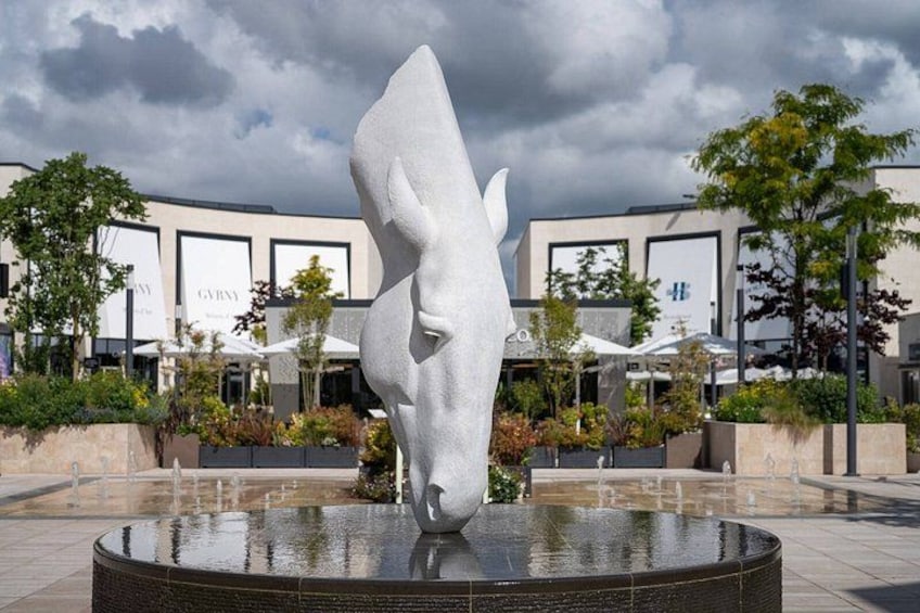 A modern sculpture of a horse's head in a fountain, surrounded by a plaza with buildings and trees. 4