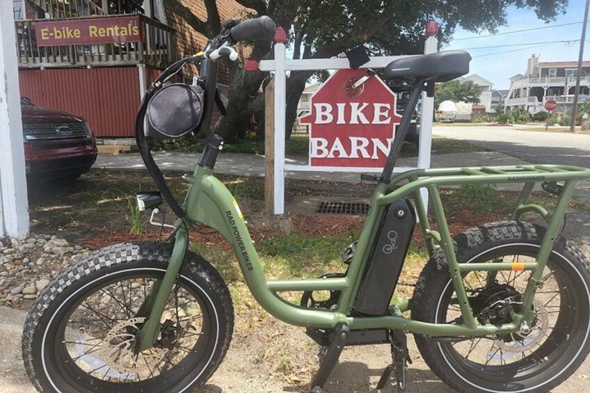 A green electric bike parked in front of a sign that reads 'BIKE BARN.' 1